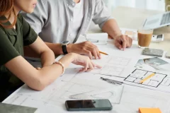 Man en vrouw zitten in een vergadering en overleggen terwijl ze kijken naar plannen op een tafel