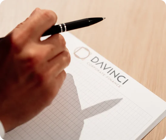 Notitieblok met het logo van DaVinci waarboven een hand met pen zweeft